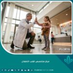 طبيب قلب أطفال يبتسم لطفلة في ردهة مركز متخصص لطب قلب الأطفال، يرمز للأمل والرعاية المتقدمة.