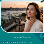 امرأة واثقة تبتسم وتلمس حنجرتها برفق بعد عملية نجاح علاج خشونة الصوت في تركيا للحصول على صوت أنثوي ناعم.