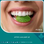 ابتسامة ناصعة البياض مع ورقة نعناع تمثل العناية بنظافة الفينير للحصول على نفس منعش ومنع رائحة الفم.