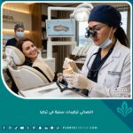 أفضل اخصائي تركيبات سنية في تركيا يفحص تاج أسنان خزفي في عيادة متطورة لتصميم الابتسامة.