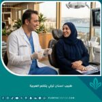 طبيب أسنان تركي يتكلم العربية يبتسم ويتحدث بارتياح مع مريض عربي في عيادة أسنان حديثة في إسطنبول.