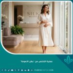 سيدة أنيقة تقف بثقة وتضع يديها على بطنها المسطح بعد إجراء عملية التخلص من بطن الأمومة في عيادة تجميل فاخرة.